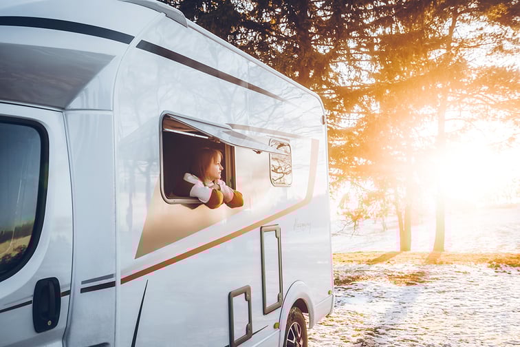 Femme dans son camping-car qui regarde le sol enneigé par la fenêtre