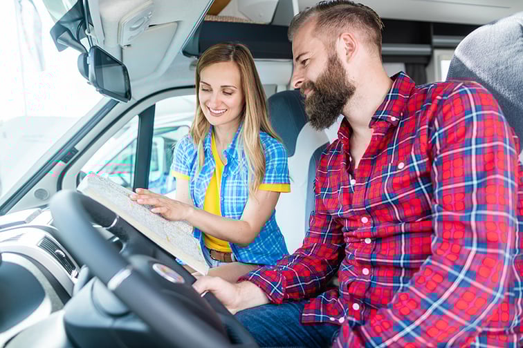 Un homme et une femme dans le poste de conduite d'un fourgon aménagé en train de regarder une carte.