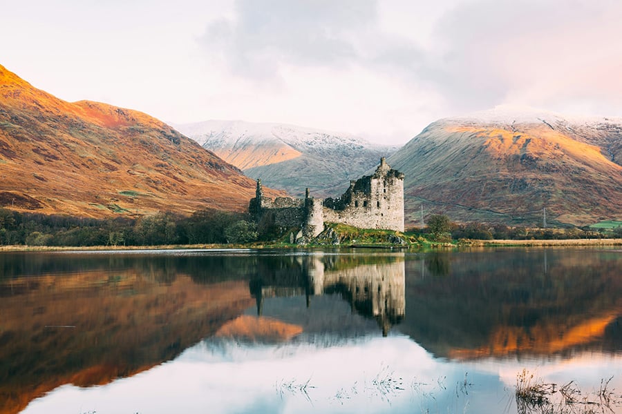 Paysage d'Ecosse : un château abandonné et des collines oranges se reflètent parfaitement sur le lac au premier plan.