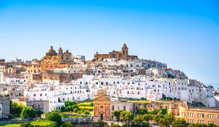 Village d'Ostuni dans les Pouilles en Italie avec de nombreuses maisons blanches et quelques monuments orangés, sous un ciel bleu.