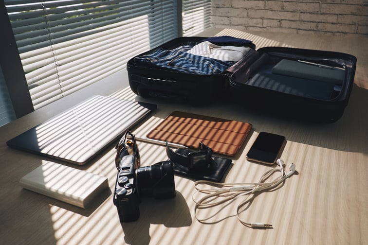 packed-suitcase-lying-desk-by-window-with-blinds-electronic-devices-nearby