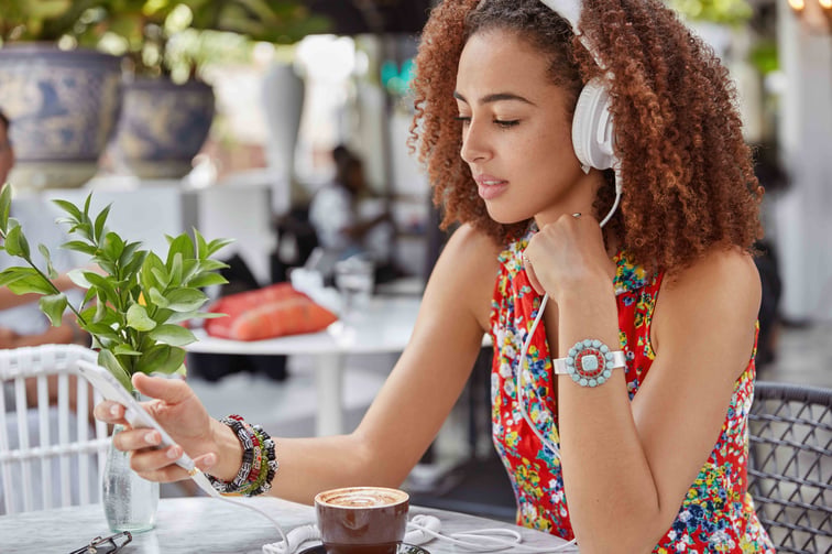 shot-beautiful-concentrated-female-has-afro-hairstyle-searches-favourite-song-playlist-enjoys-loud-music-headphone-while-sits-outdoor-cafeteria
